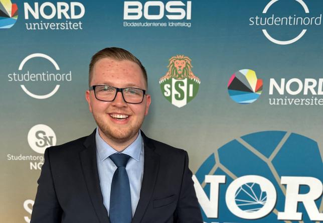 Håvard Dragland ikledd dress foran fotovegg for Nord Cup