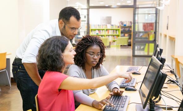 Three students in foront of a computer at a library