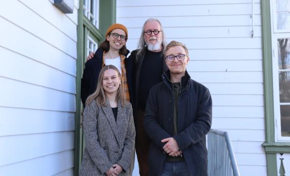 Fire personer står i en trapp foran et hvitt bygg. Tre menn og en kvinne. 