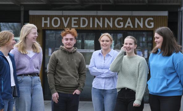 Seks mennesker på rekke og rad foran en hovedinngang. Foto