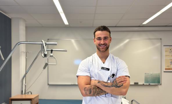 Mannlig sykepleierstudent med sykepleier uniform smiler mot kamera.