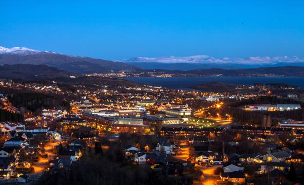 Dronebilde av by og landskap sett fra luften i kveldsmørke.