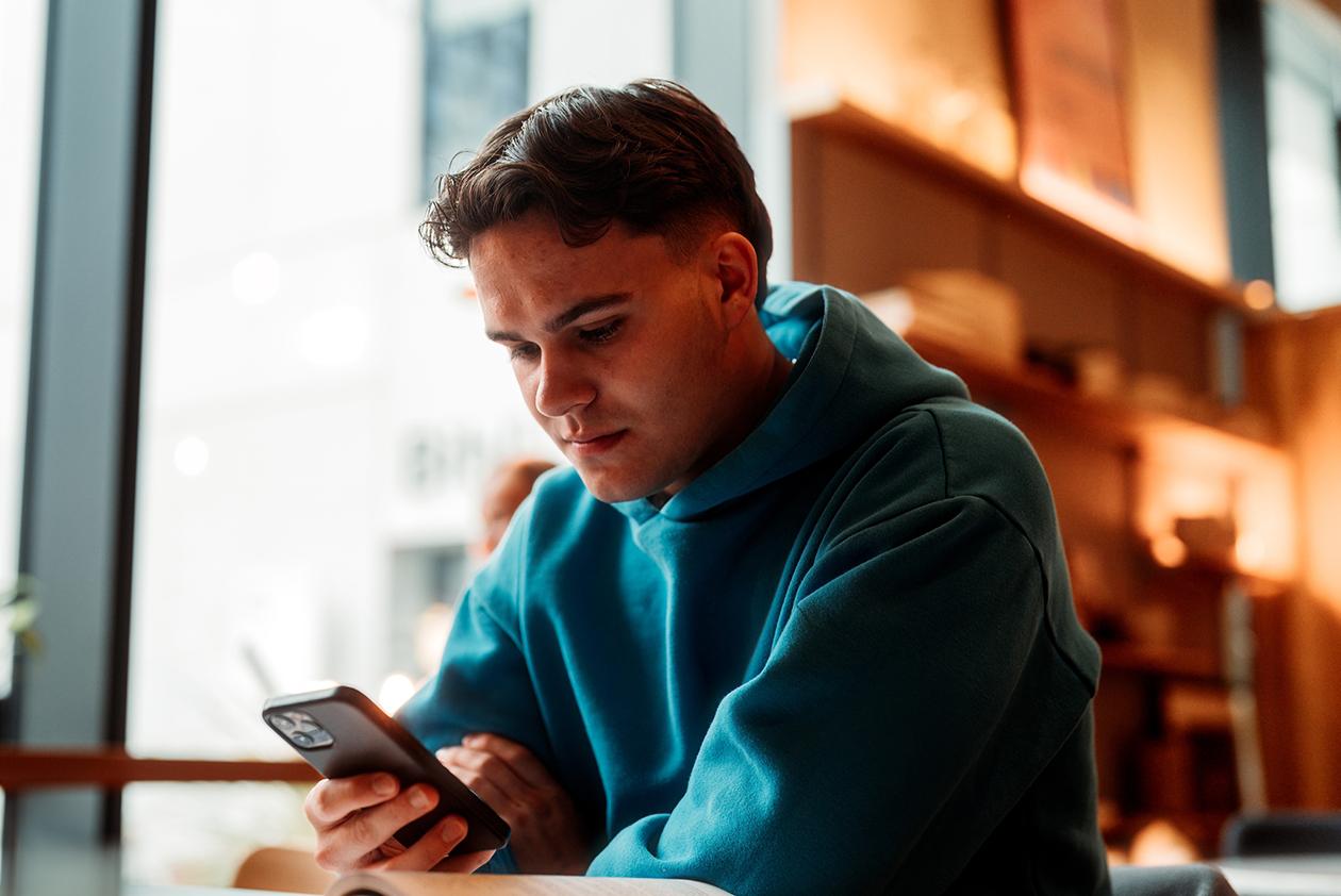 Student med grønn hettegenser ser i mobil