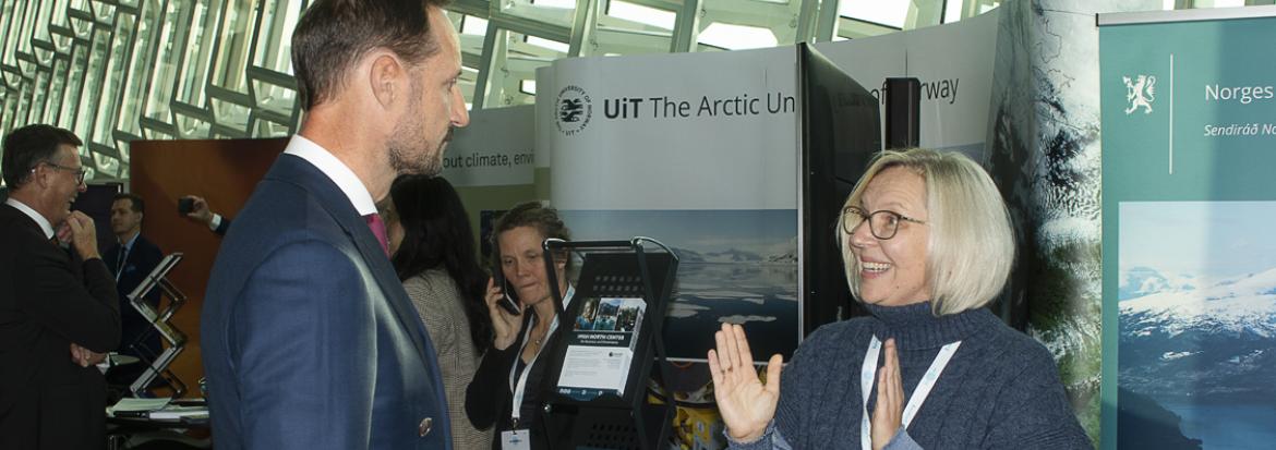 Førsteammanuensis Elena Dybtsyna gestikulerer og snakker med Kronprins Haakon på en stand under konferanse