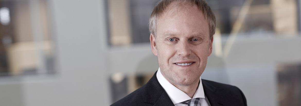 Portrettbilde av voksen mann i dressjakke, skjorte og med slips. Foto