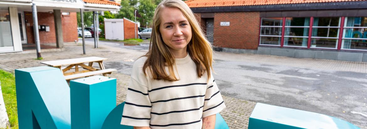 Ung kvinne ute foran bokstaver og bygninger. Foto