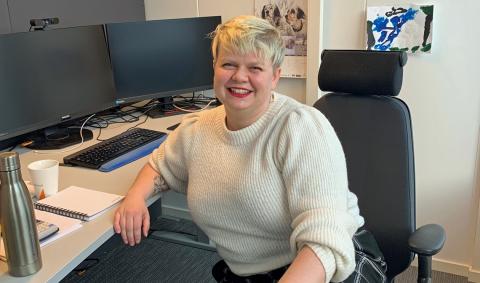 Smilende kvinne foran PC på arbeidsplass.