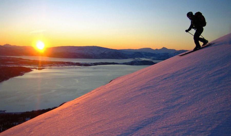 Skiløper på vei ned fjellside i solnedgang.