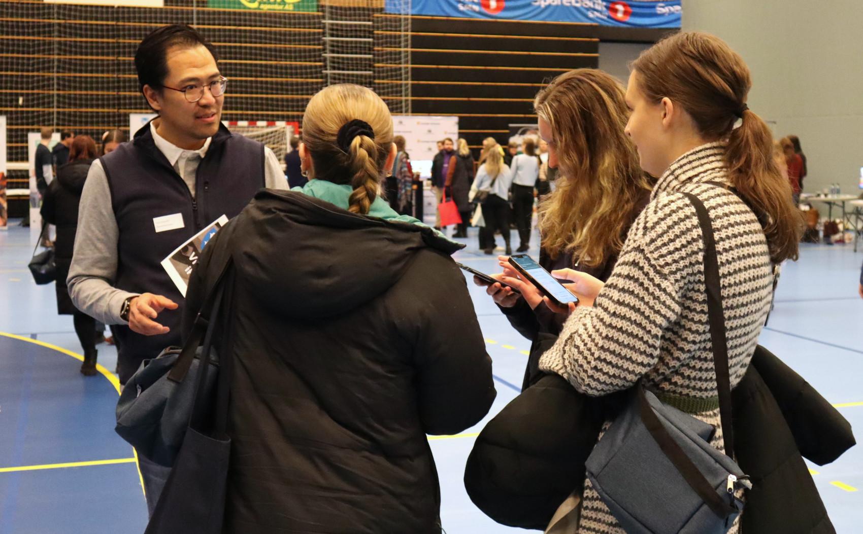 Tre unge kvinner står rundt en mann som holder opp en plakat