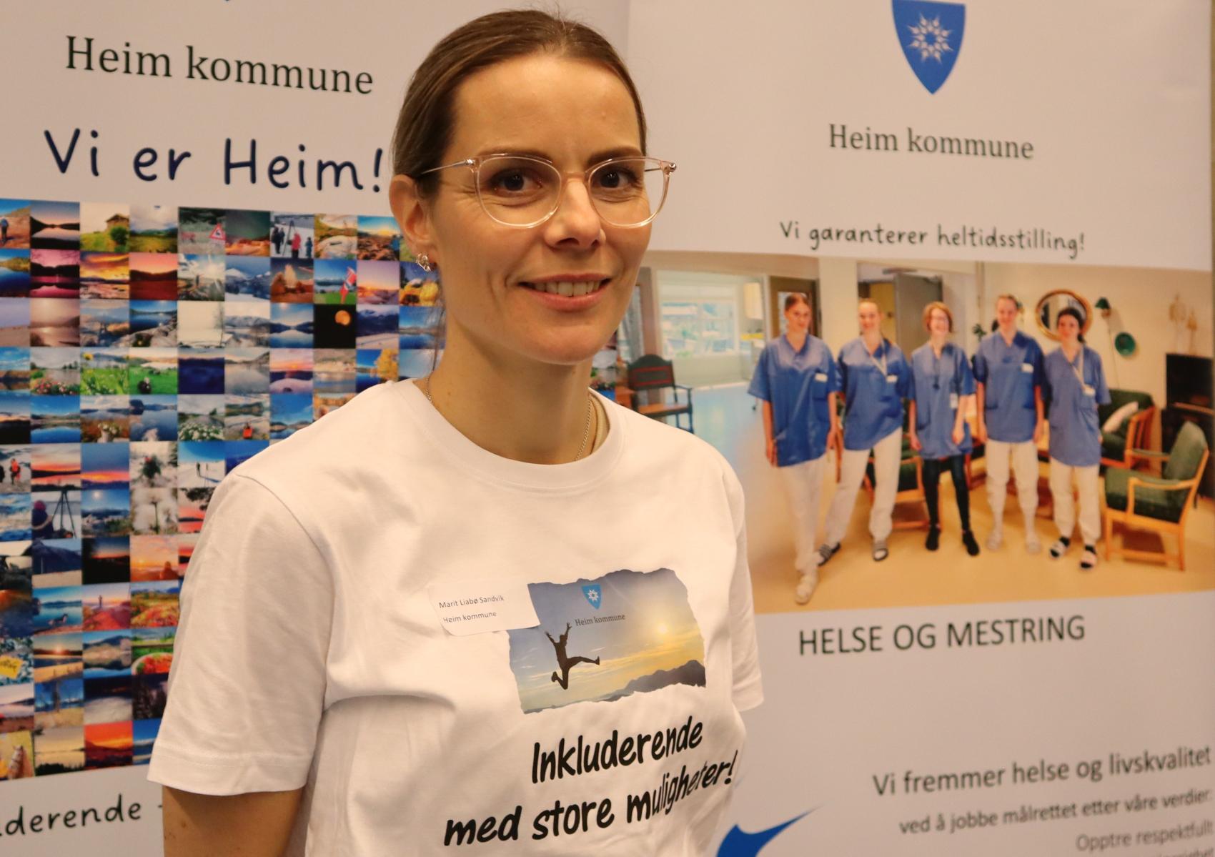 Nærbilde av dame med briller foran rollups med reklame for Heim kommune