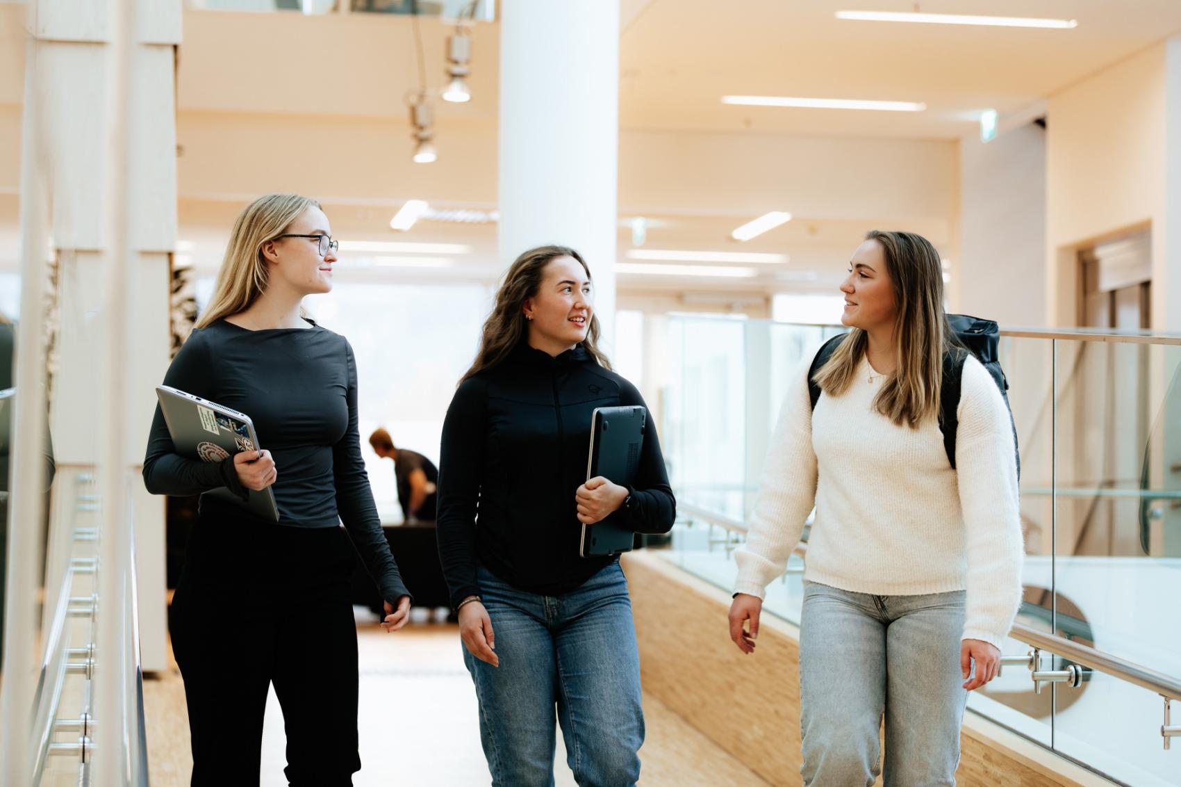 Tre studenter går og snakker i en gang. Foto.