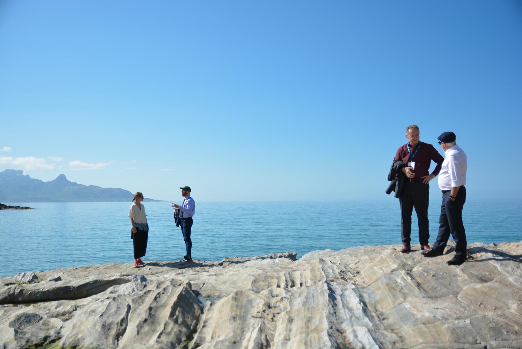 4 people standing by the sea, two and two talking to each other. Sunny weather