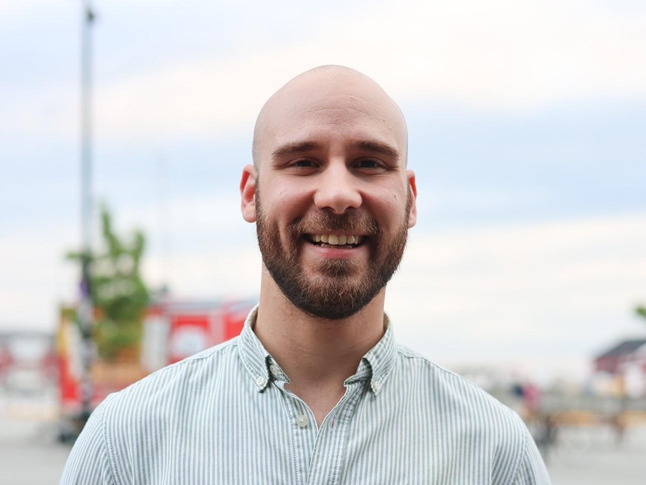 A portrait of a smiling man. He holds a plastic glass in his hand. 