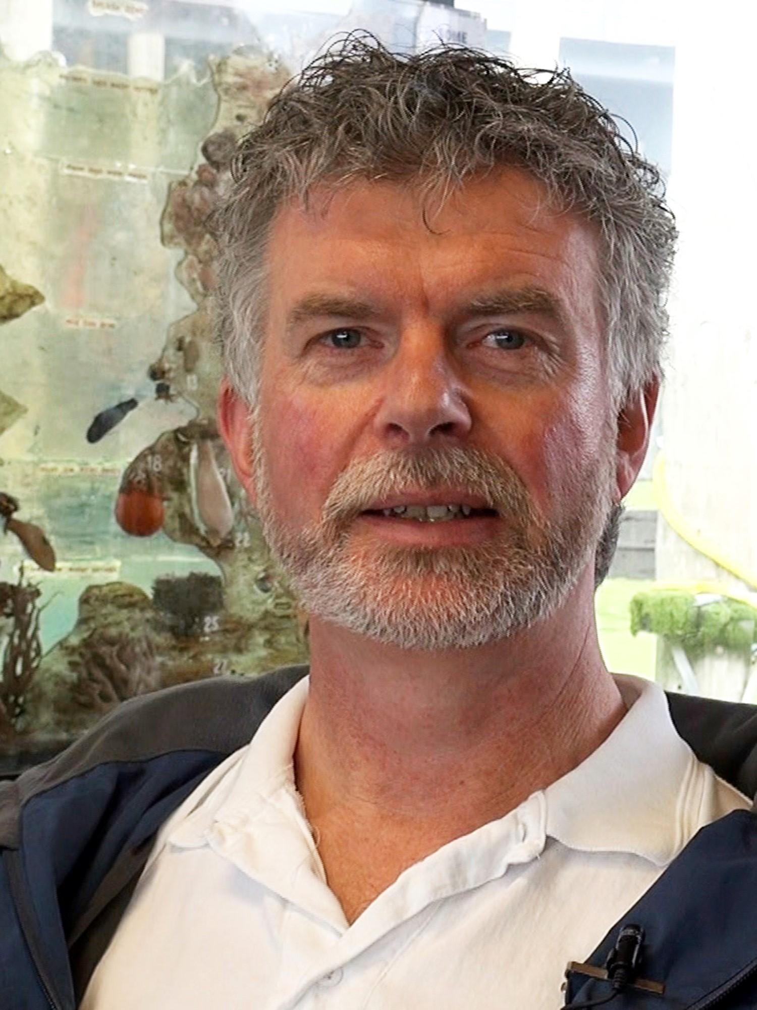 Portrettbilde av mann med grålig krøllete hår, litt skjegg og bart