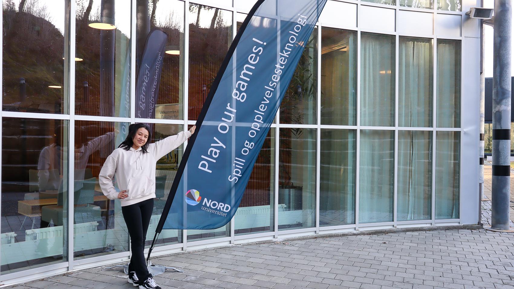 Smilende ung kvinne i lys genser holder i et beachflagg med teksten "play our games". 