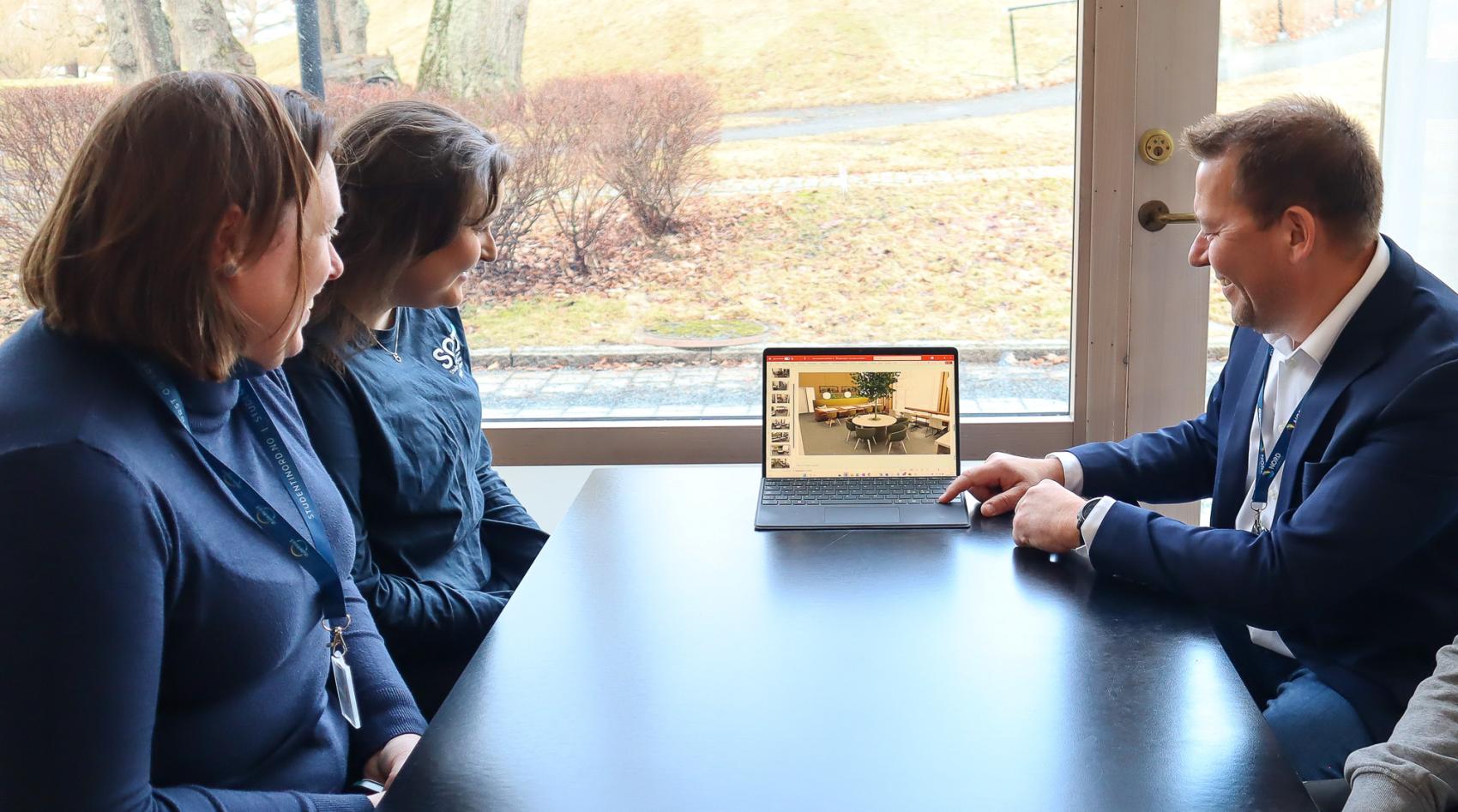 Tre personer sitter rundt et bord og ser på en PC-skjerm med bilde av møbler