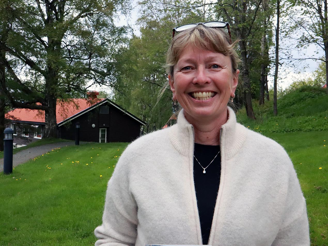 Portrettbilde av kvinne i hvit genser ute i en park med grønt gress bak. Foto