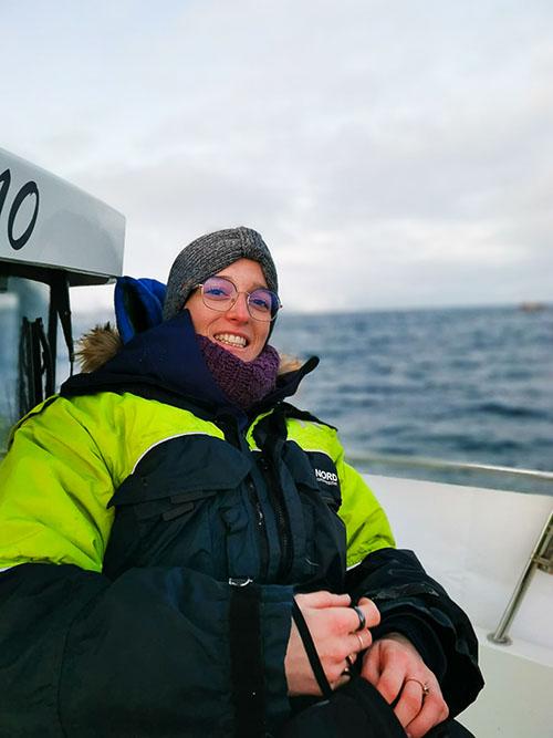 Portrettbilde av ung kvinne med tykk kjeldedress ombord i en båt på det åpne hav. Foto