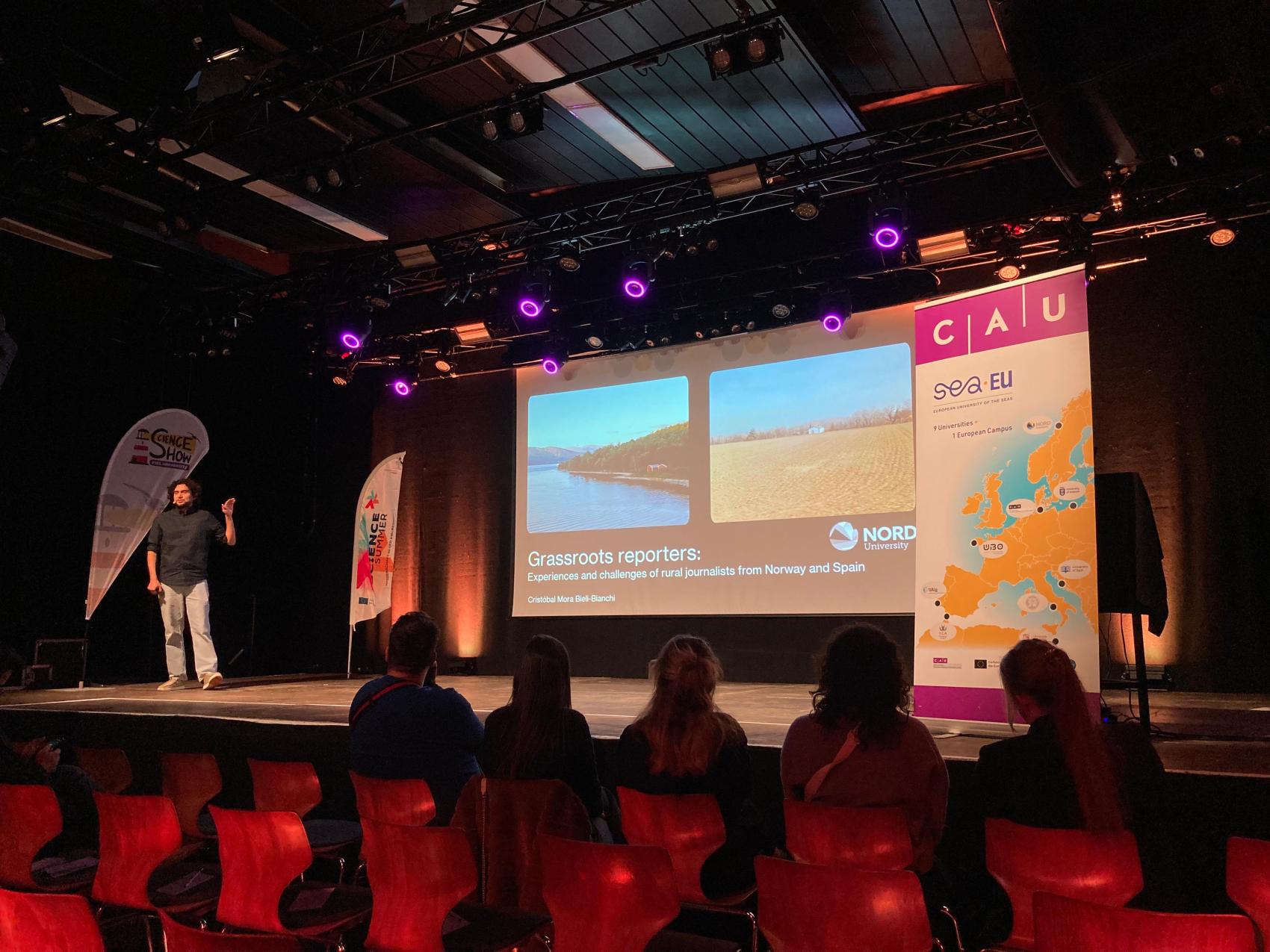 Man stands on a stage, presenting a project with slides on the screen