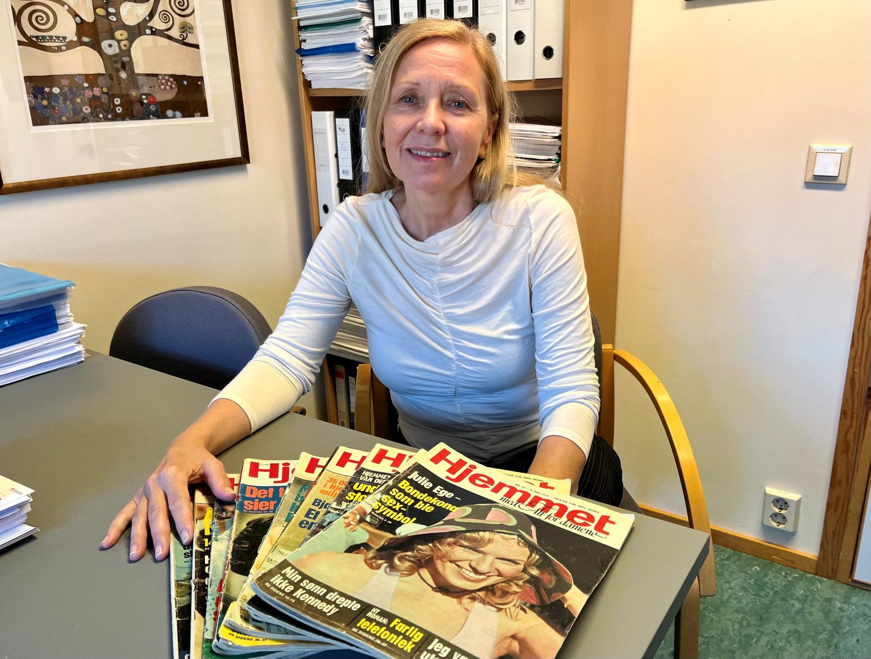 Kvinne ved bord foran ein bunke med ukeblad. Foto