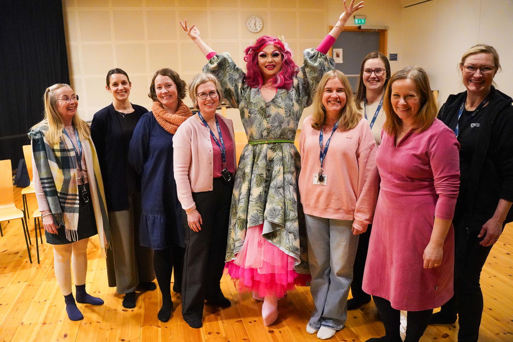 Gruppebilde av ti mennesker med en dragartist i midten. Foto