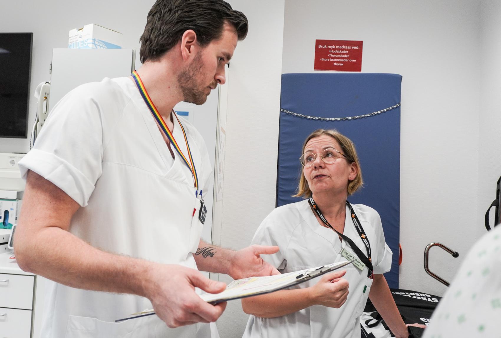 Mannlig sykepleier som diskuterer med en kvinnelig sykepleier. Foto