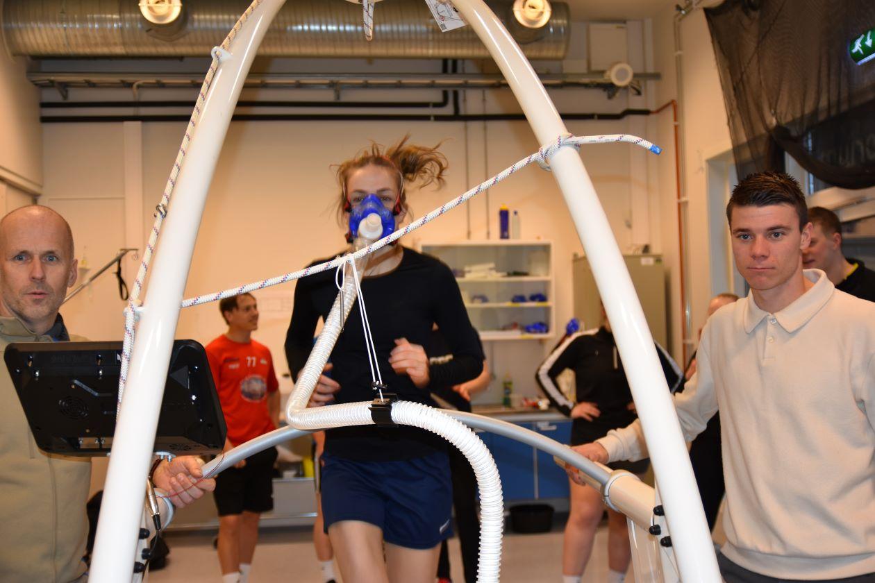 Jente som løper på mølle med oksygenmaske. To lærere ved siden av. Foto