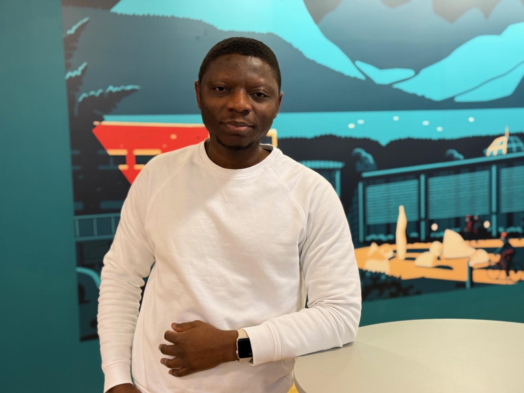 Voksen mann i hvit genser foran en vegg med maleri. Foto