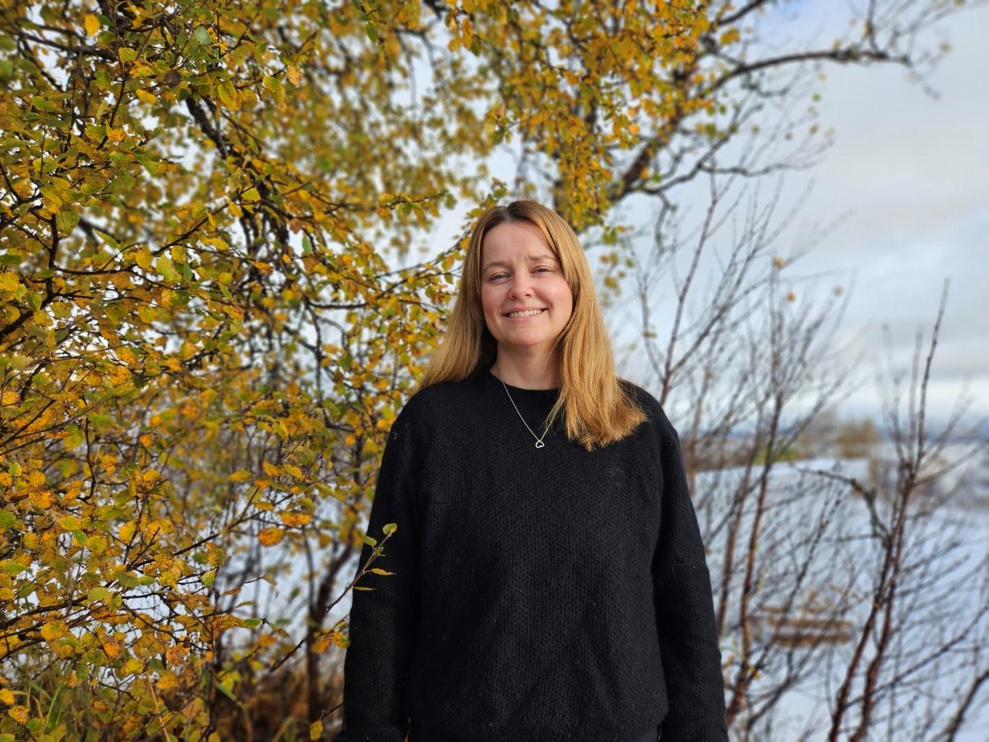 Kvinne ute ved bjørketre i godt høstlys