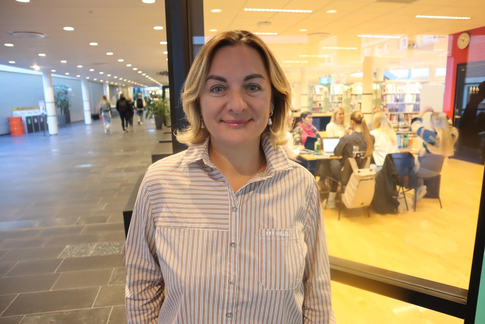 Kvinne i skjorte inne i gang, med mennesker bak. Foto