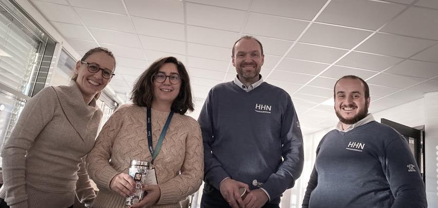 To kvinner til venstre og to menn til høyre som står i en gang og ser ned i kamera