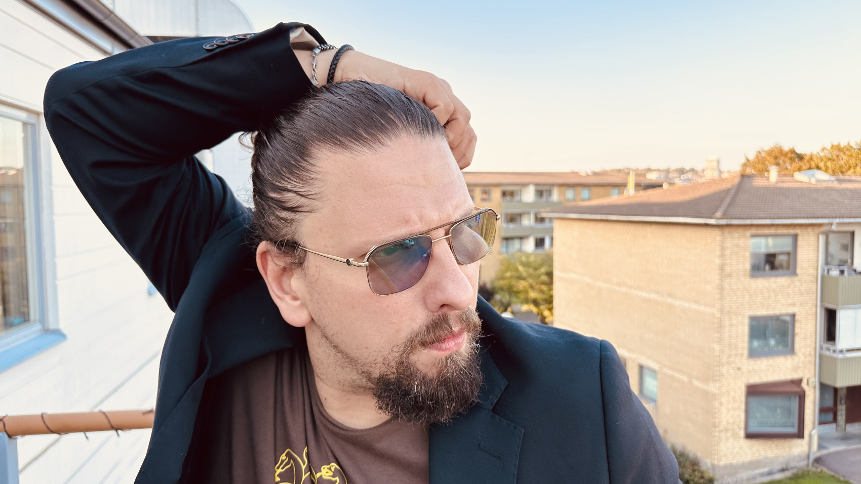 Nærbilde av mann med solbriller og glattkjemmet hår ute på veranda. Foto