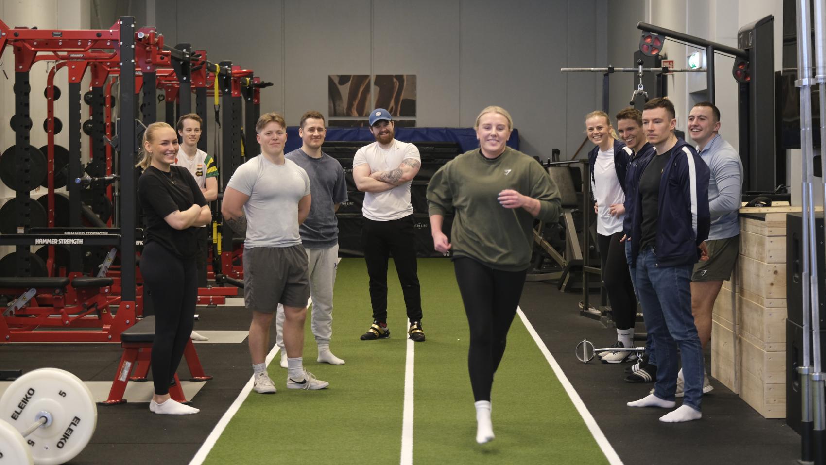 Ung jente som løper mot kamera inne i treningssal, med mange mennesker rundt. Foto