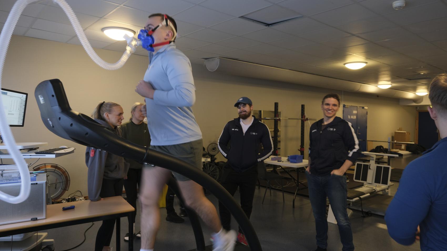 Mann som løper på mølle med oksygenmaske, med flere mennesker rundt. Foto