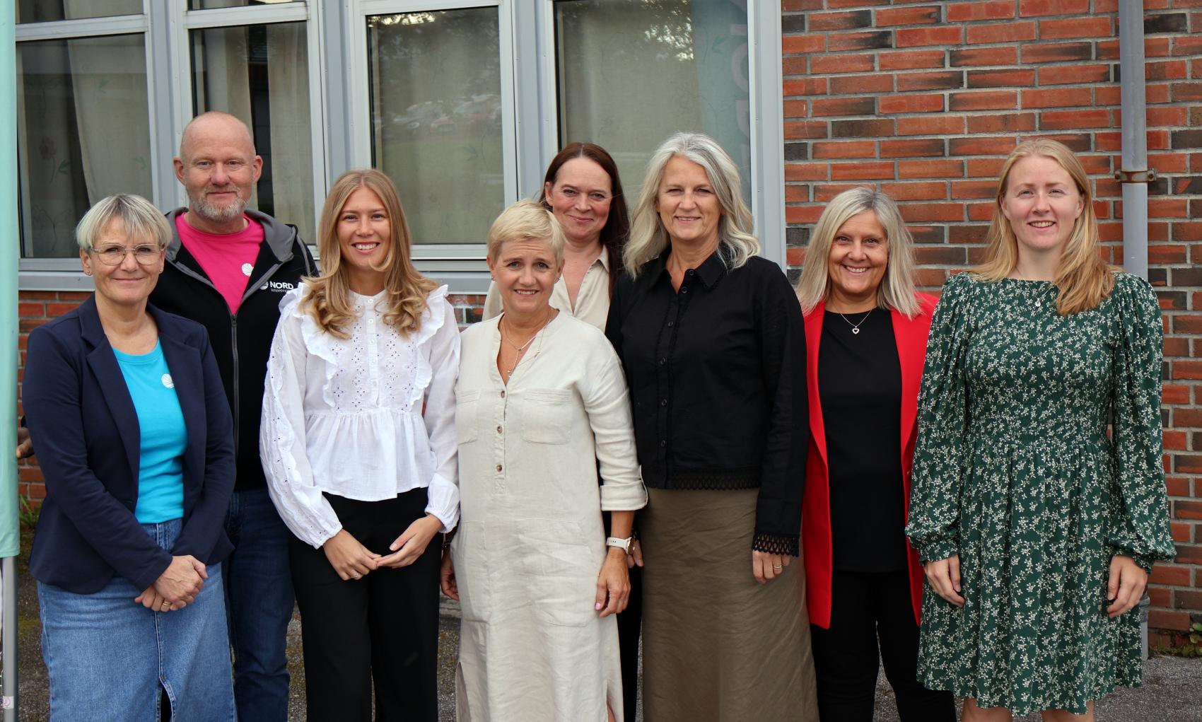 Åtte voksne mennesker foran murbygning. Foto