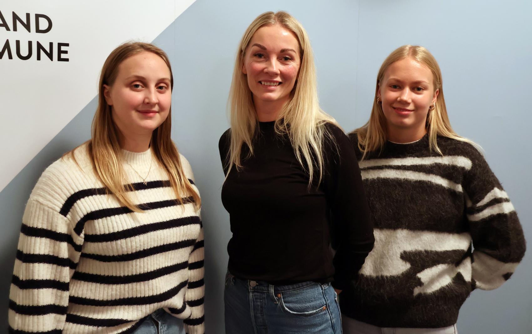 Tre kvinner som står mot en vegg